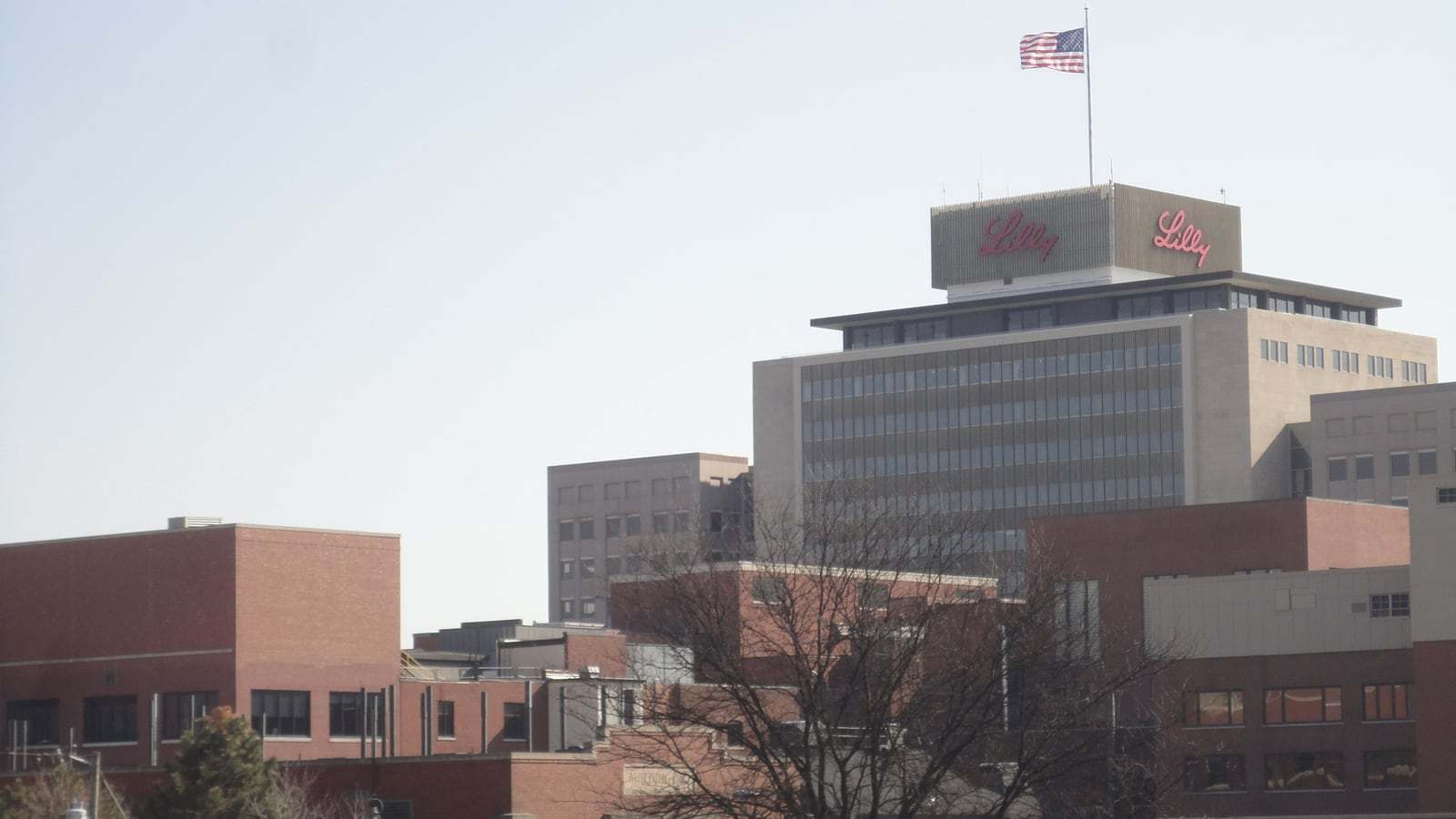 An office tower topped with the red Lilly logo rises above brick buildings at Eli Lilly and Company's Indianapolis campus