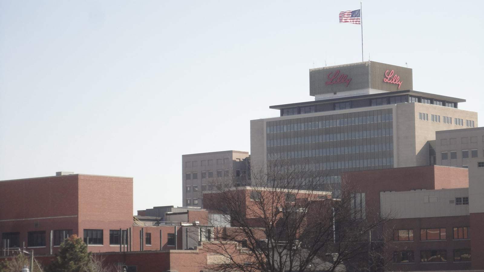A multi-story brick and glass Eli Lilly corporate building in Indianapolis with a circular driveway and landscaped lawn in the foreground.