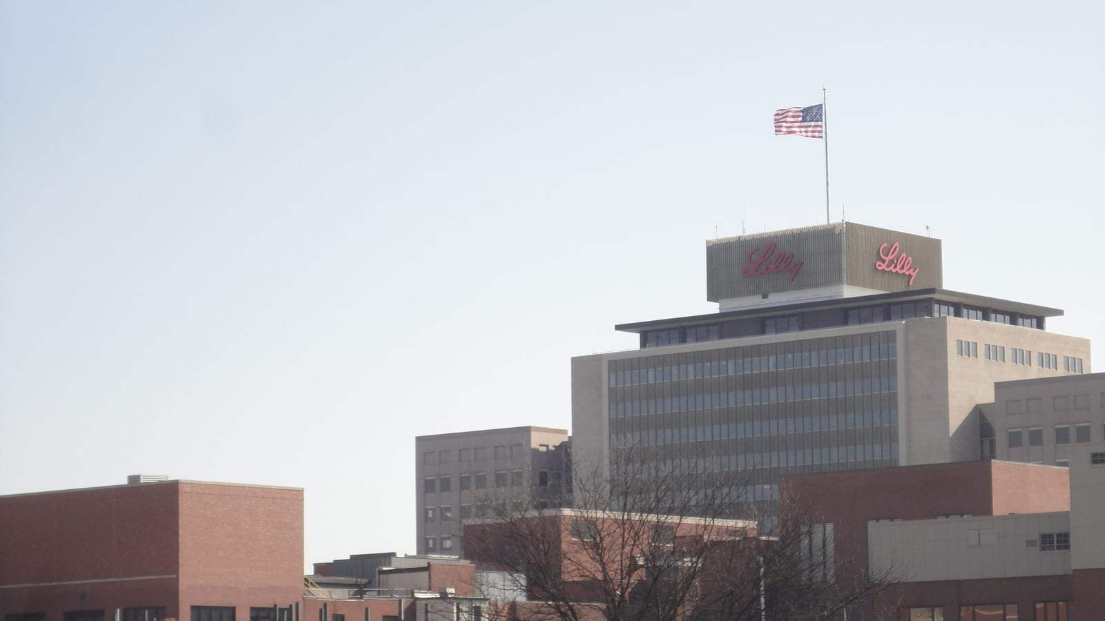 A multi-story brick and glass Eli Lilly corporate building in Indianapolis with a circular driveway and landscaped lawn in the foreground.