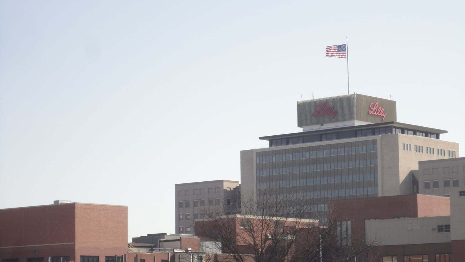 A multi-story brick and glass Eli Lilly corporate building in Indianapolis with a circular driveway and landscaped lawn in the foreground.